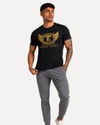 My Store ATHLEX Forged Legacy black cotton tee with gold warrior emblem graphic worn by a man in grey joggers