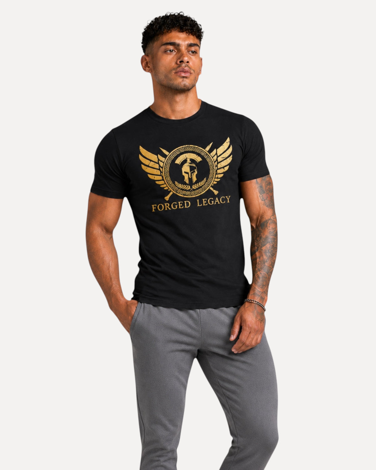 My Store ATHLEX Forged Legacy black cotton t-shirt with gold warrior helmet graphic worn by a man in grey joggers